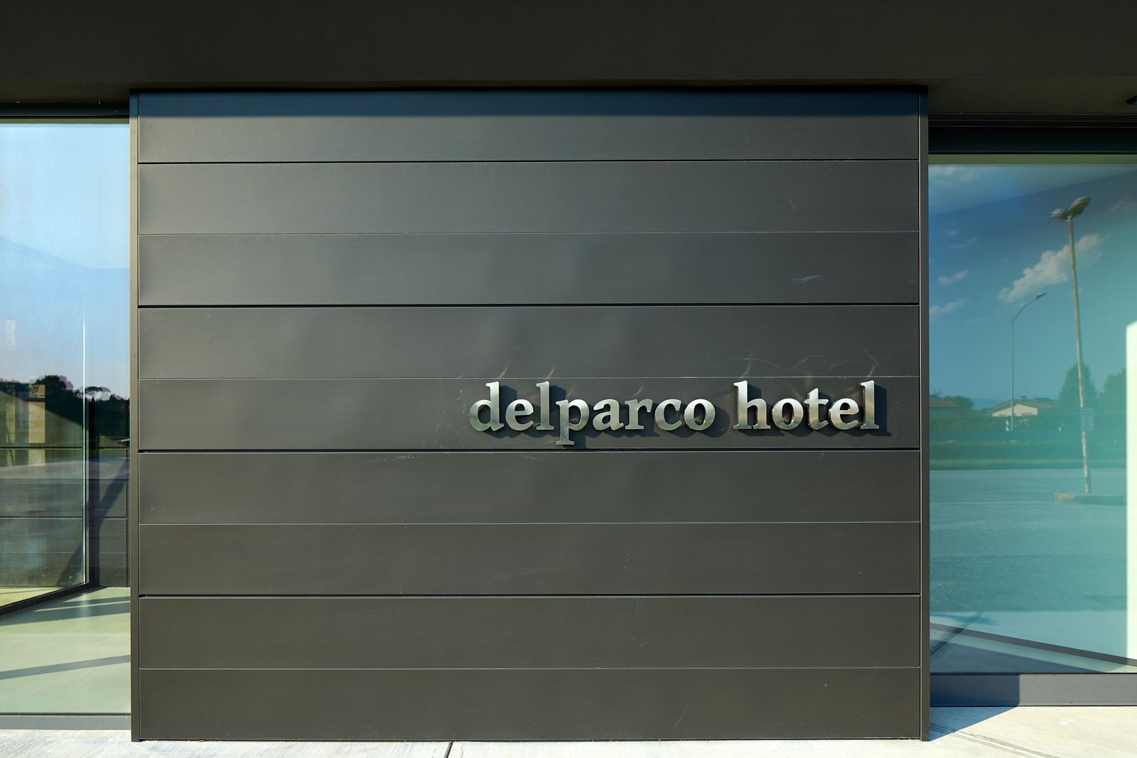 Placa de hotel moderna com o nome 'delparco hotel' exibido em letras metálicas sobre fundo escuro.