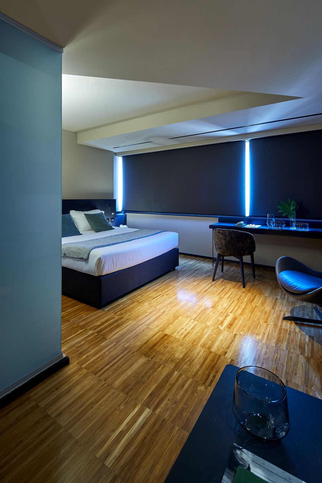 Een moderne slaapkamer met een bed, bureau, stoel en een glas water op een tafel.