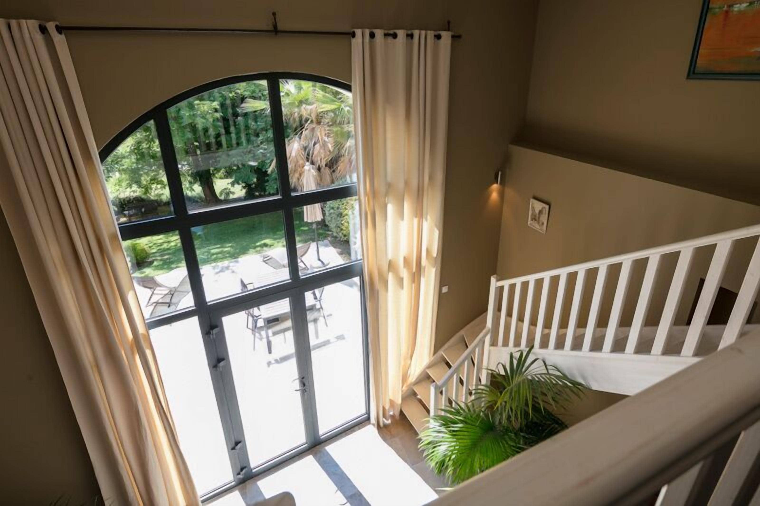 A view from a window with a view of a patio area, a white railing, and a potted plant.