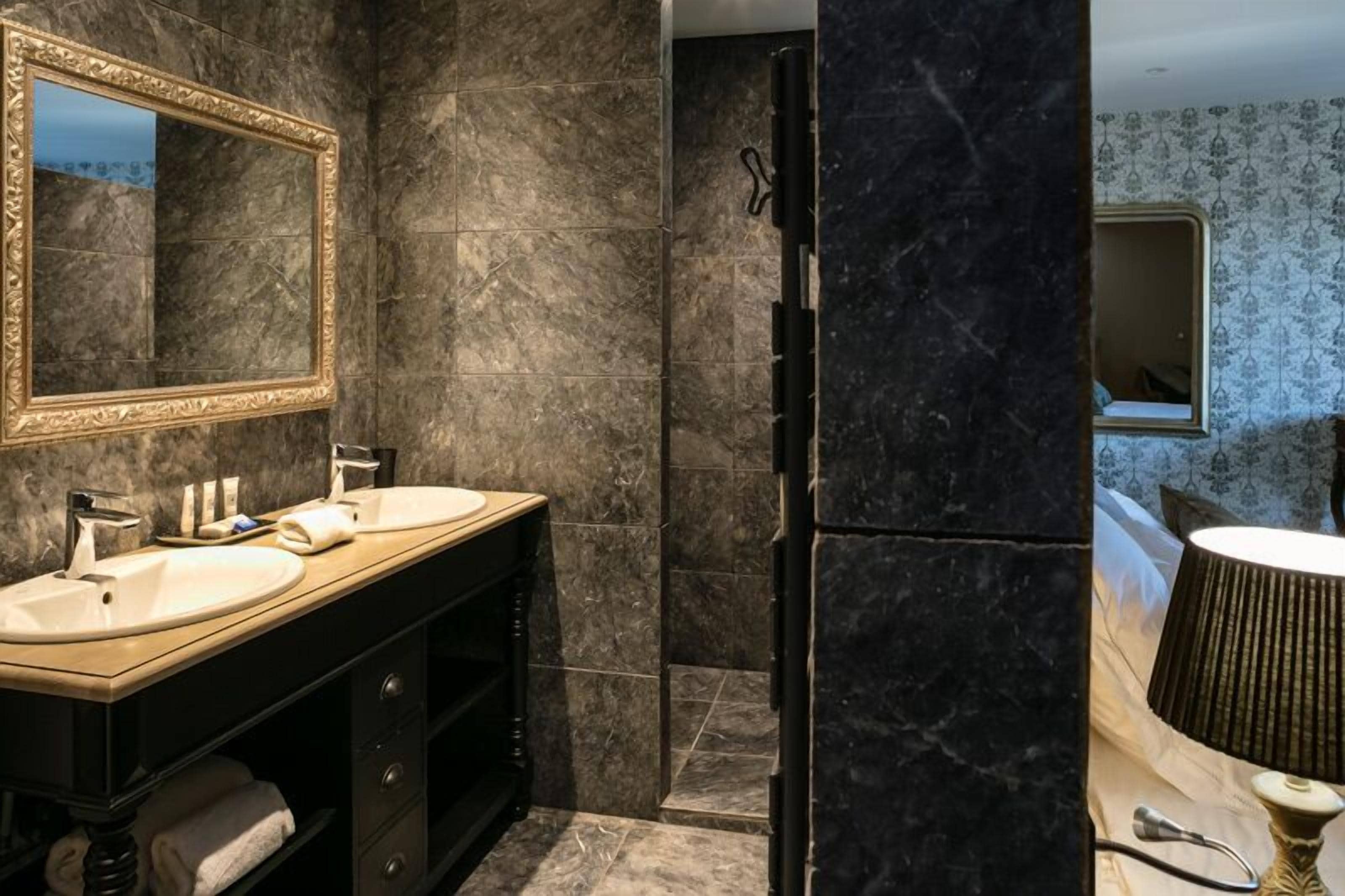 A modern bathroom with two sinks, a large mirror, and dark marble walls.