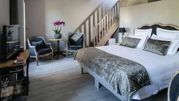 Slaapkamer met een groot bed, een stoel, een kleine tafel met een plant, een lamp en een trap.