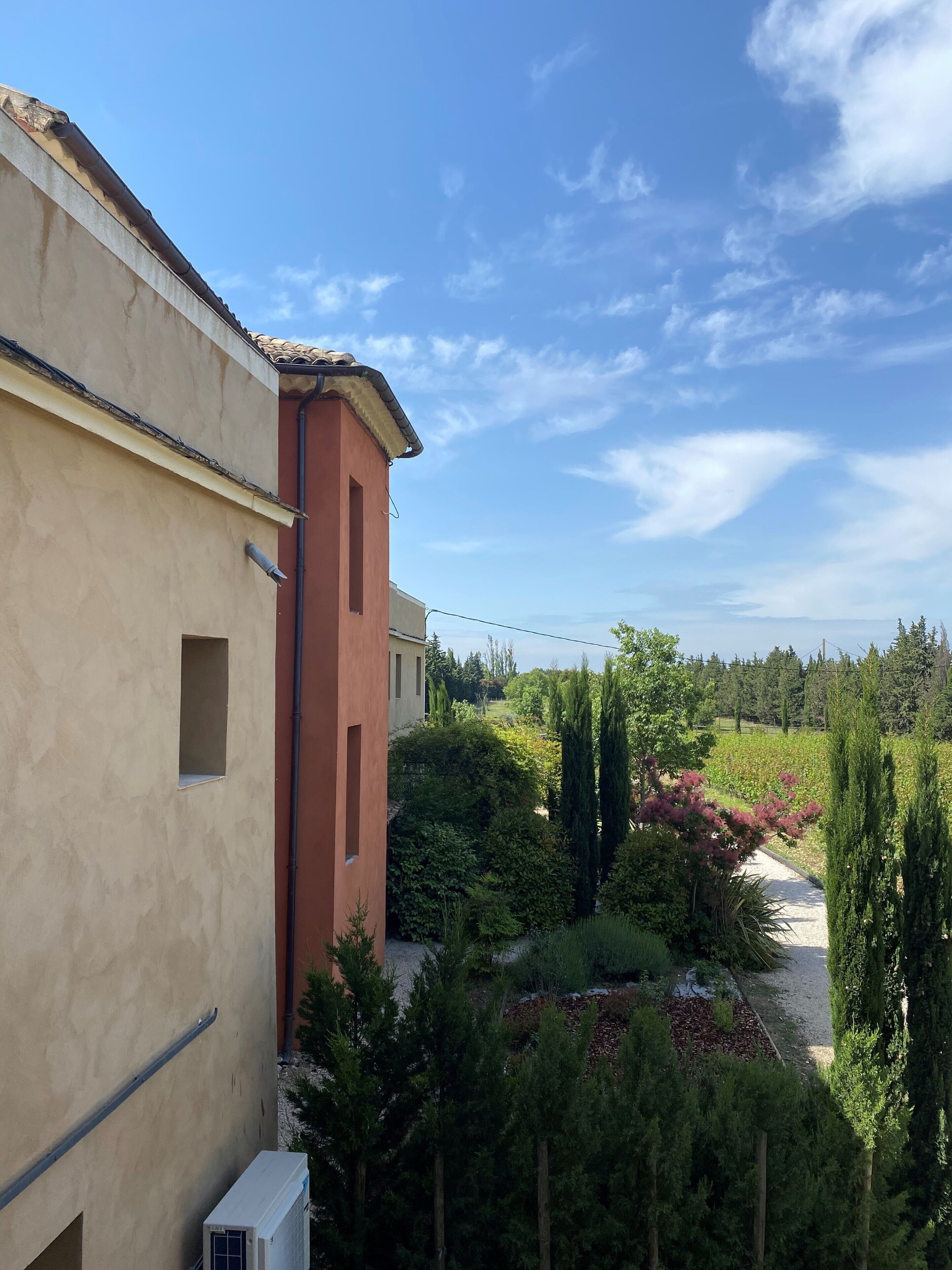 Ein Gebäude mit beiger Fassade und rotem Bereich, umgeben von einem Garten mit verschiedenen Pflanzen und einem Kiesweg.