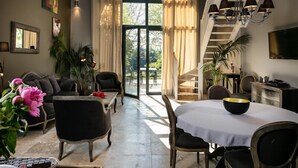 Amplia sala de estar con sofá, mesa de comedor y sillas, una escalera que lleva a un área exterior, y un televisor montado en la pared.
