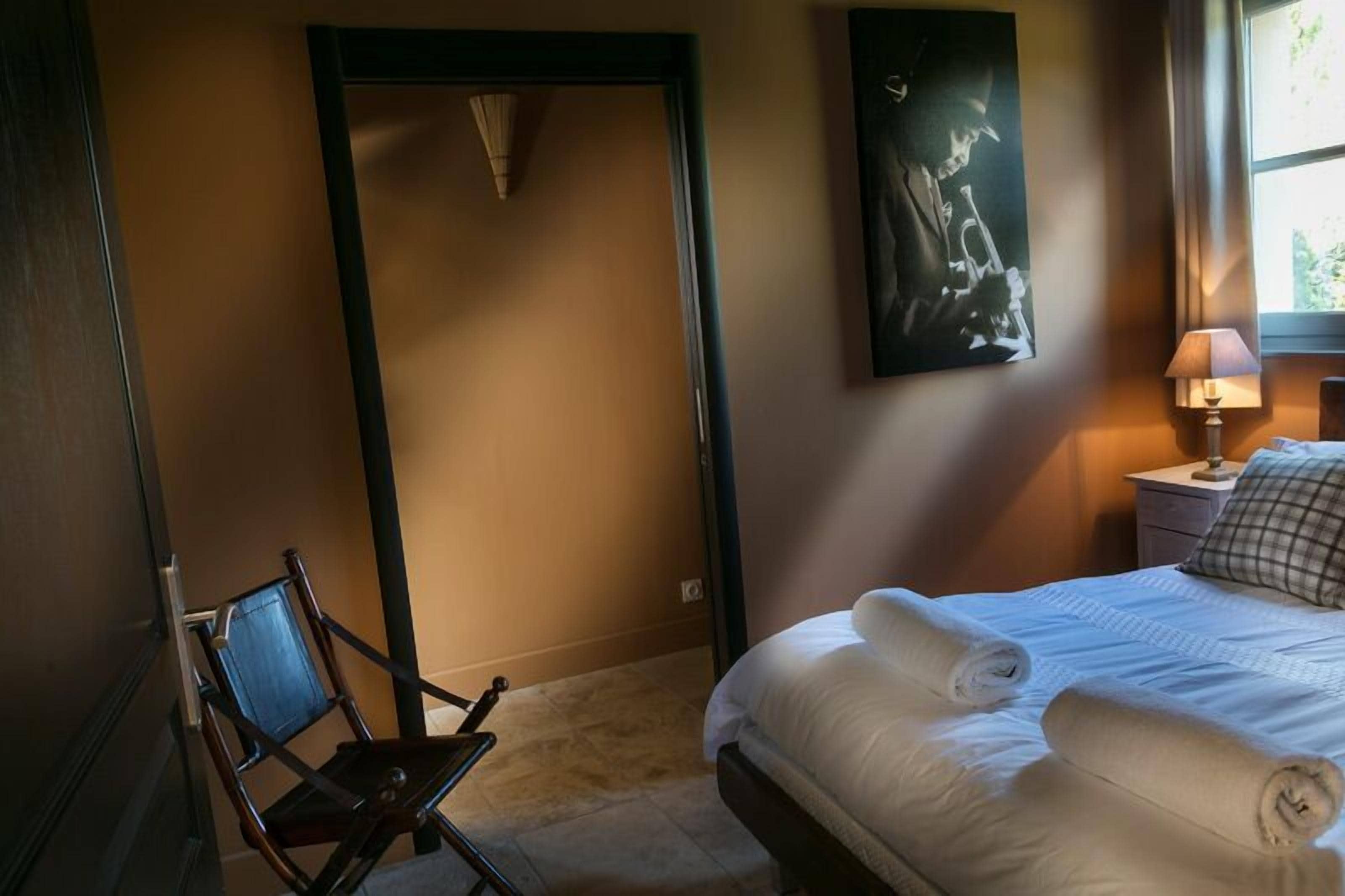 Een hotelkamer met een bed, een stoel, een schilderij aan de muur en een raam met gordijnen.