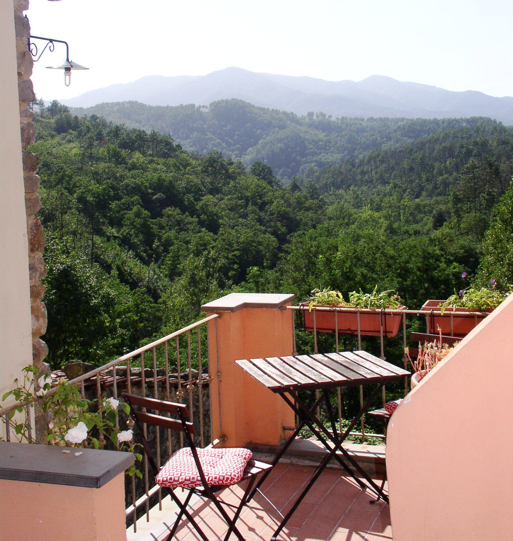Varanda com mesa e cadeiras, com vista para um vale arborizado e montanhas distantes.