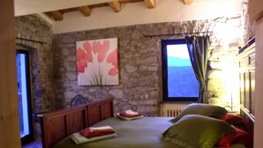 A bedroom with a stone wall, a bed with green bedding, a painting, and a window with a view. - B&B Il Tulipano (Ricco del Golfo di Spezia)