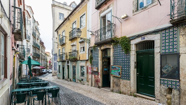 Une ruelle étroite pavée, bordée d’immeubles présentant une architecture portugaise traditionnelle, notamment des façades décorées de carreaux de céramique et des balcons.