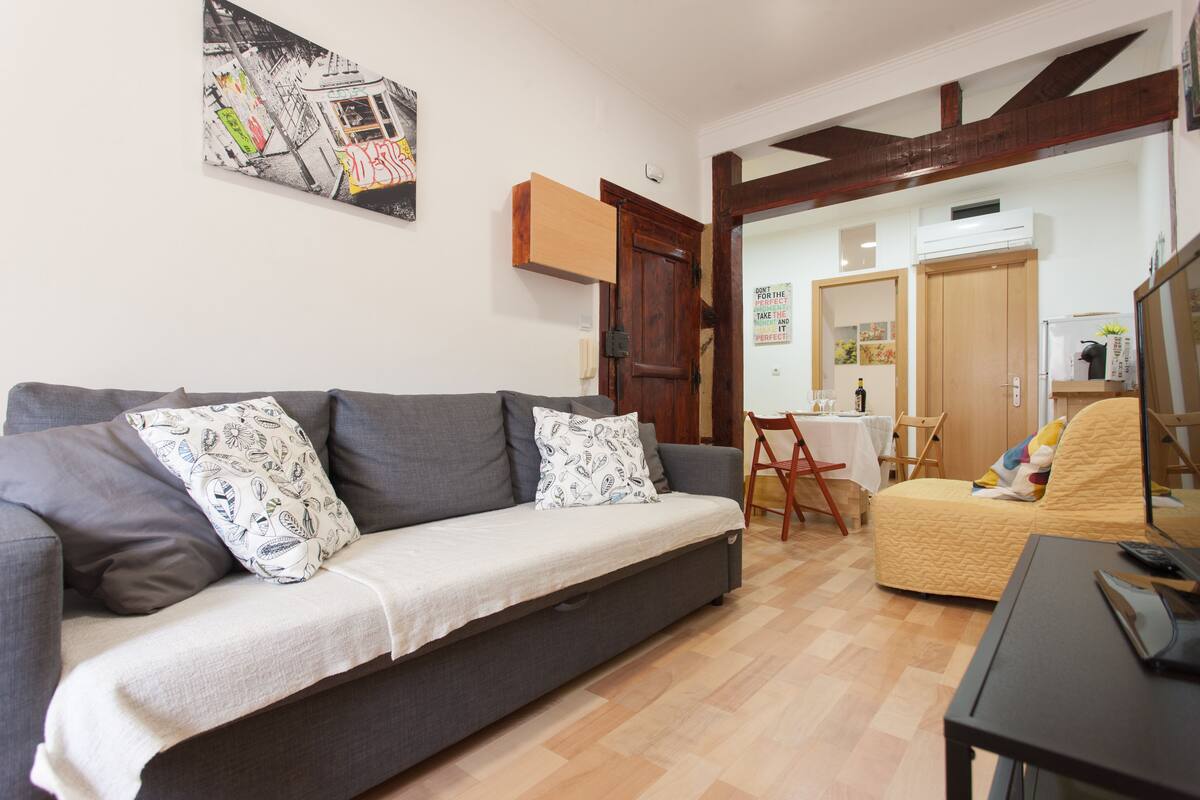 Un salon avec un canapé gris, un fauteuil jaune et une table à manger avec des chaises.