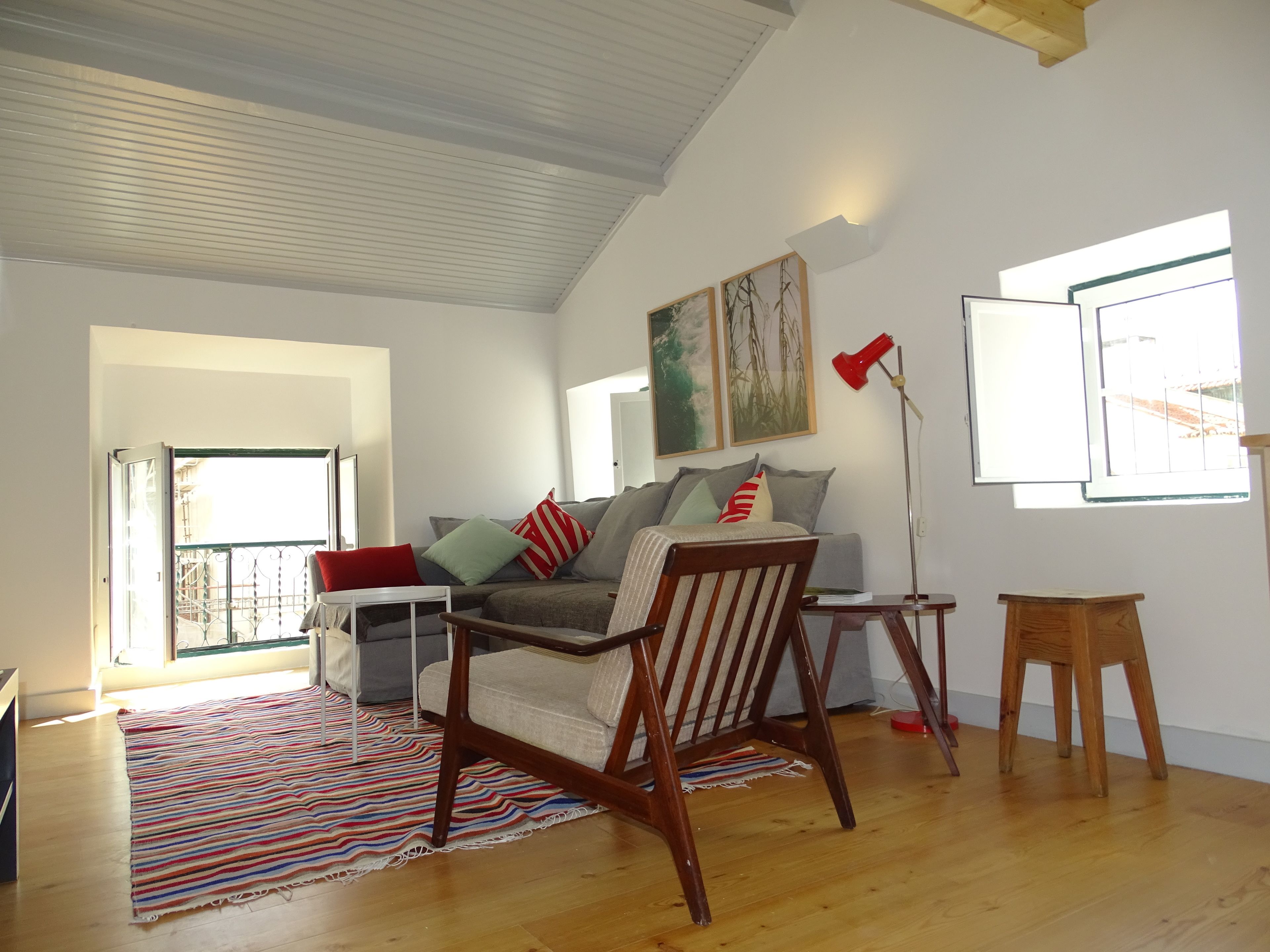 A living room with a wooden floor, a sofa, a chair, a small table, and a window with a view of the outside.
