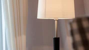 A lamp with a white shade and a black base, positioned next to a curtain tied back with a knot.