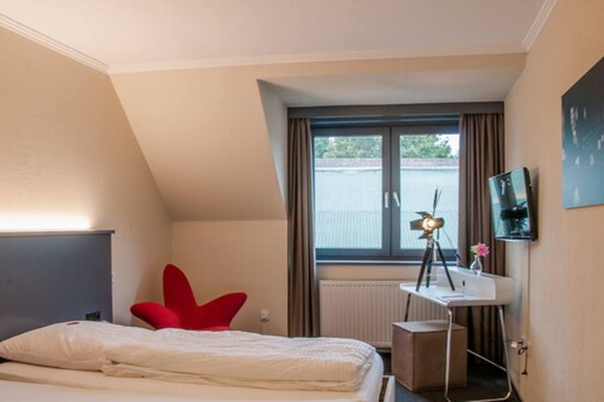A bedroom with a bed, a desk with a lamp, a chair, and a window with curtains.
