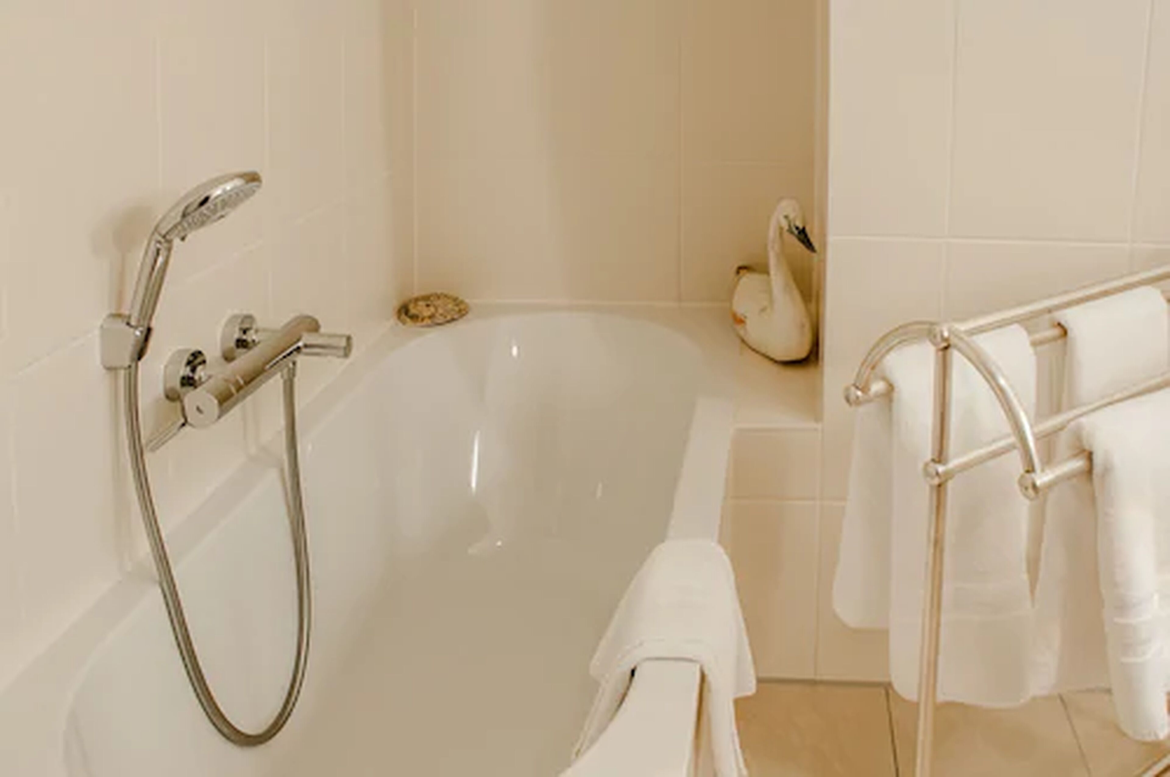 A modern bathroom with a bathtub, a handheld showerhead, and a towel rack with towels.