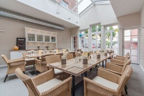 A spacious dining area with high ceilings and large windows, featuring wicker furniture and a modern kitchen in the background. - Kino - Hotel Meyer (Harsefeld)