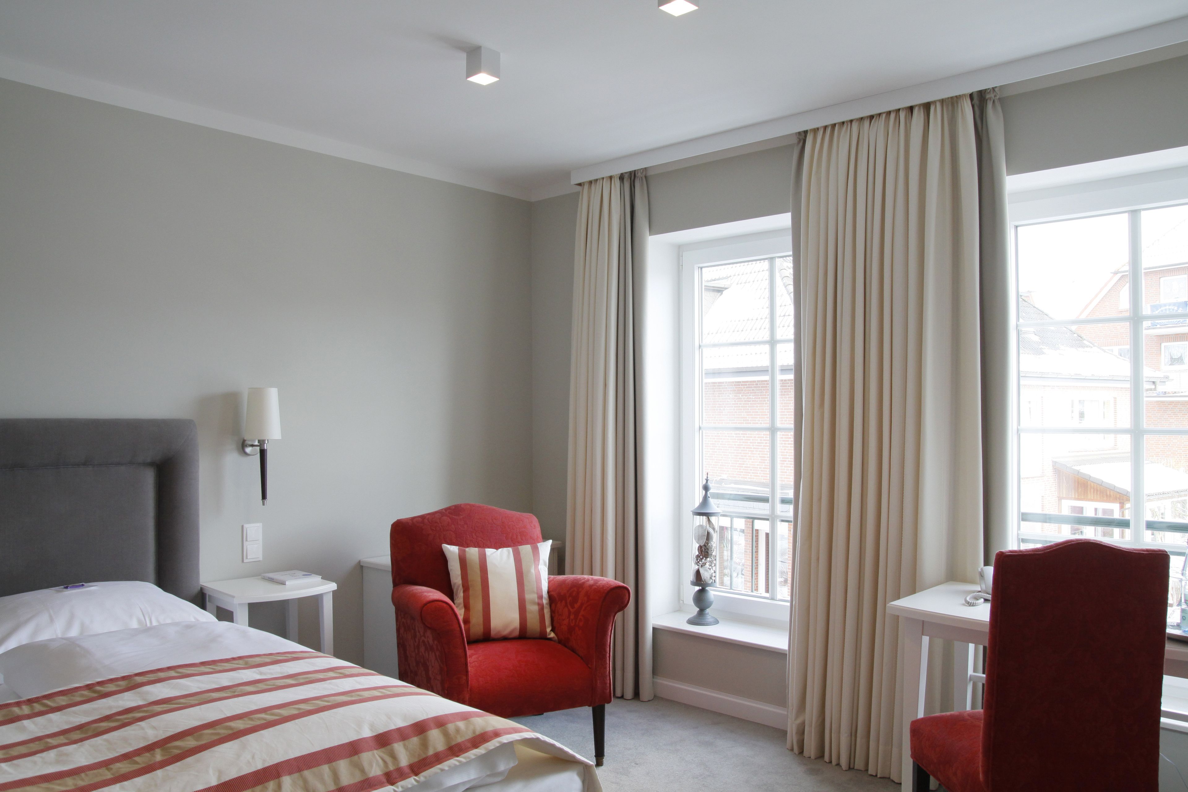 Una habitación de hotel con cama, un sillón rojo, una mesita y una ventana con cortinas.