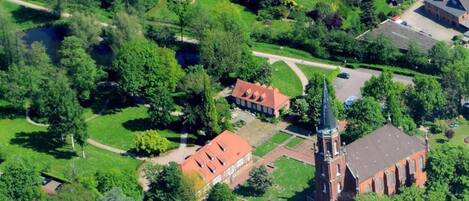 An aerial view of a residential area with a prominent red-roofed building, likely a church, surrounded by lush greenery and a well-maintained lawn.