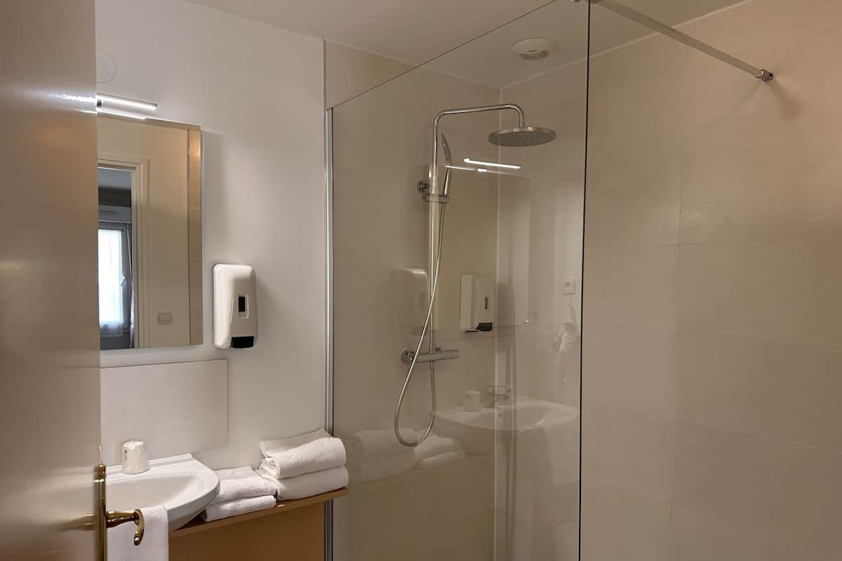 Een moderne badkamer met een douchecabine van glas, een wastafel met handdoekhouder en een spiegel.
