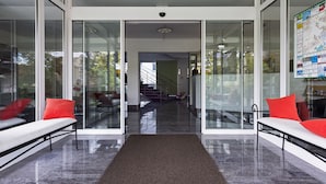 A modern interior with glass doors leading to a staircase and a seating area with red cushions. - BIG Reisehotel Wolfen (Bitterfeld-Wolfen)