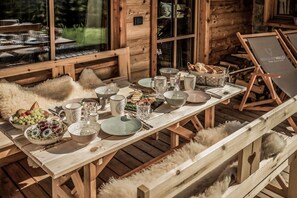 Ein Holzespeisetisch, gedeckt mit Tellern, Schüsseln, Gläsern und einem Brotkorb, in einer rustikalen Holzhütte.