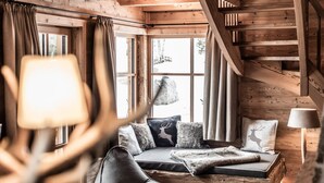 Interior acogedor de una cabaña con escalera de madera, un sofá con una manta de piel sintética y una lámpara.