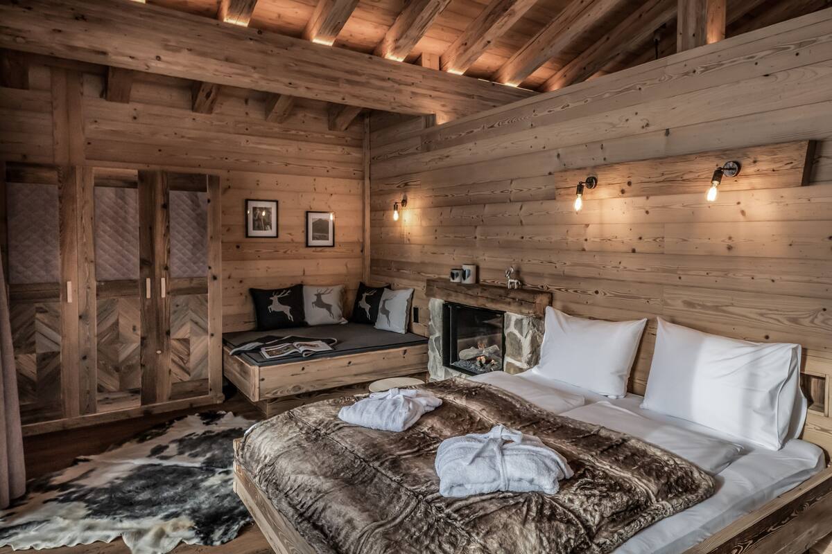 Un dormitorio de cabaña de troncos acogedor, con cama, chimenea, paredes de madera y un ventanal grande.