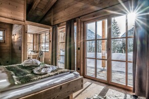 Ein gemütliches Holzhütten-Zimmer mit einem Bett, großen Fenstern und Blick auf verschneite Berge.