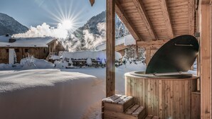 Una cabaña de madera con sauna, rodeada de montañas nevadas y un cielo despejado.
