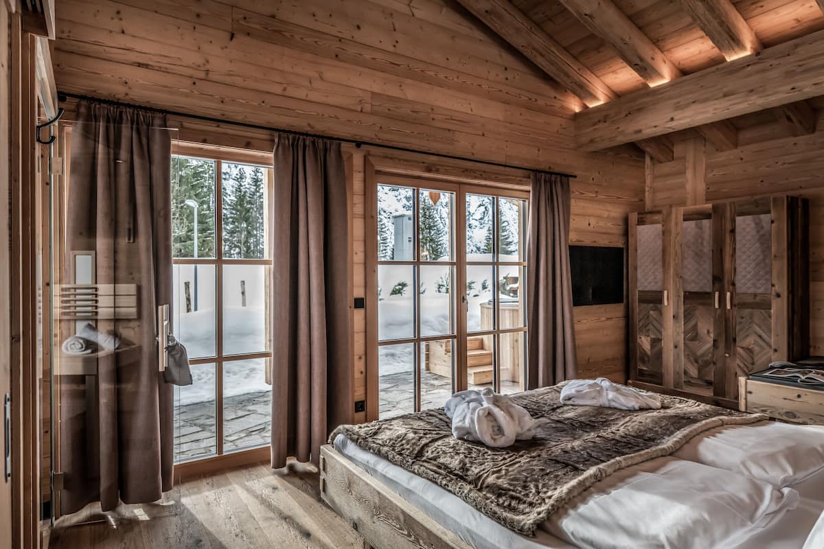 Habitación de cabaña de madera con cama, cortinas y vistas a un paisaje nevado.