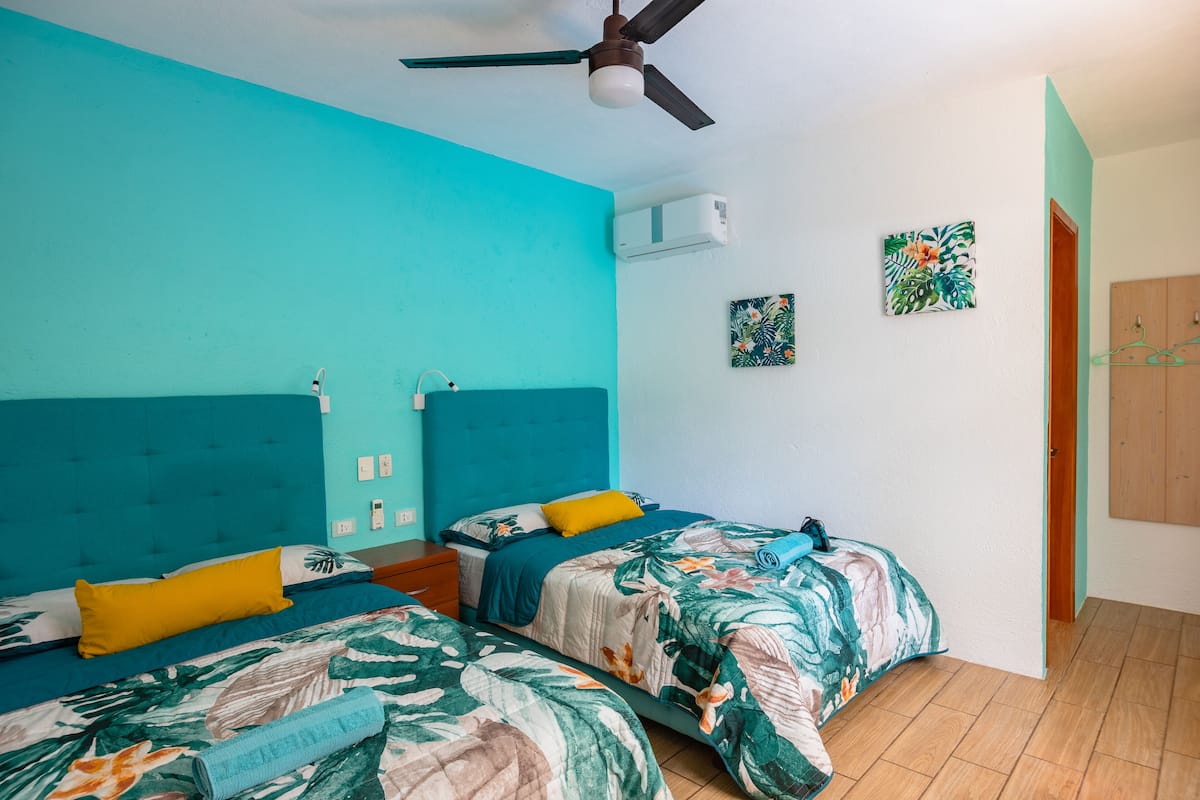 Un dormitorio con dos camas, ventilador de techo, aire acondicionado y armario de madera.