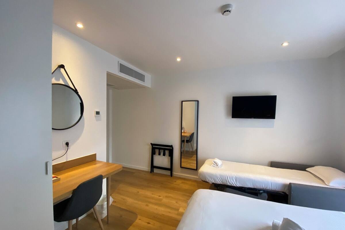 A modern hotel room with a wooden desk, a bed, a TV, and a mirror.
