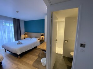 A modern hotel room with a large bed, bedside tables, a desk, and a bathroom visible through an open door. - Oskar Hotel (Annemasse)
