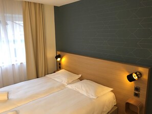 A hotel room with a large bed, two bedside lamps, a wooden headboard, and a geometric-patterned wall. - Oskar Hotel (Annemasse)