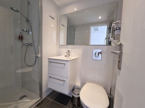 A modern bathroom with a glass-enclosed shower, a white sink with a mirror above, a toilet, and a trash bin. - Oskar Hotel (Annemasse)