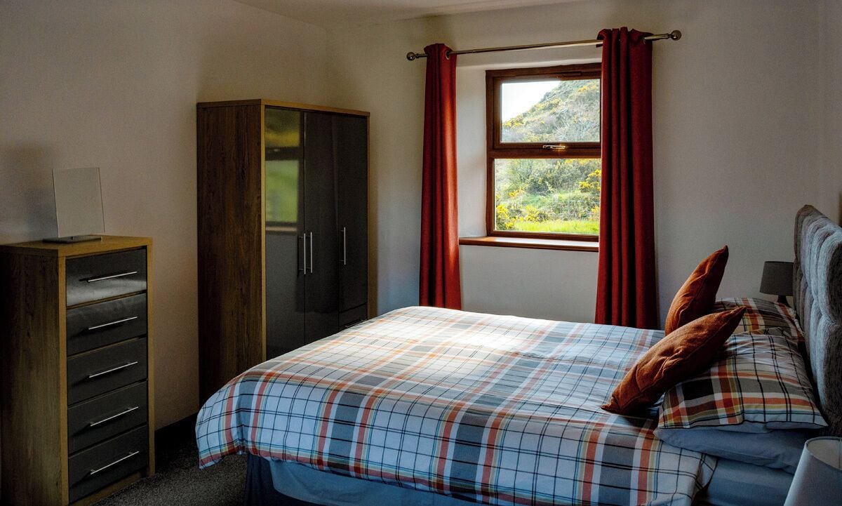 A bedroom with a bed, a wardrobe, a window with curtains, and a view of greenery outside.