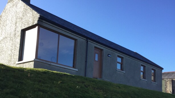 A modern house with a large window, a chimney, and a door. - Makem's Self Catering Cottage (Ballycastle)