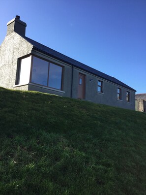 A modern house with a large window, a chimney, and a door. - Makem's Self Catering Cottage (Ballycastle)