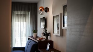 En moderne stue med en mørkeblå sofa, et træbord og en lille plante. To hængende lamper hænger over bordet, og et stort vindue er dækket af lette gardiner.
