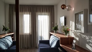 En moderne stue med sofa, sofabord og fjernsyn. Gardiner, en plante og en vase med blomster er også i rummet.