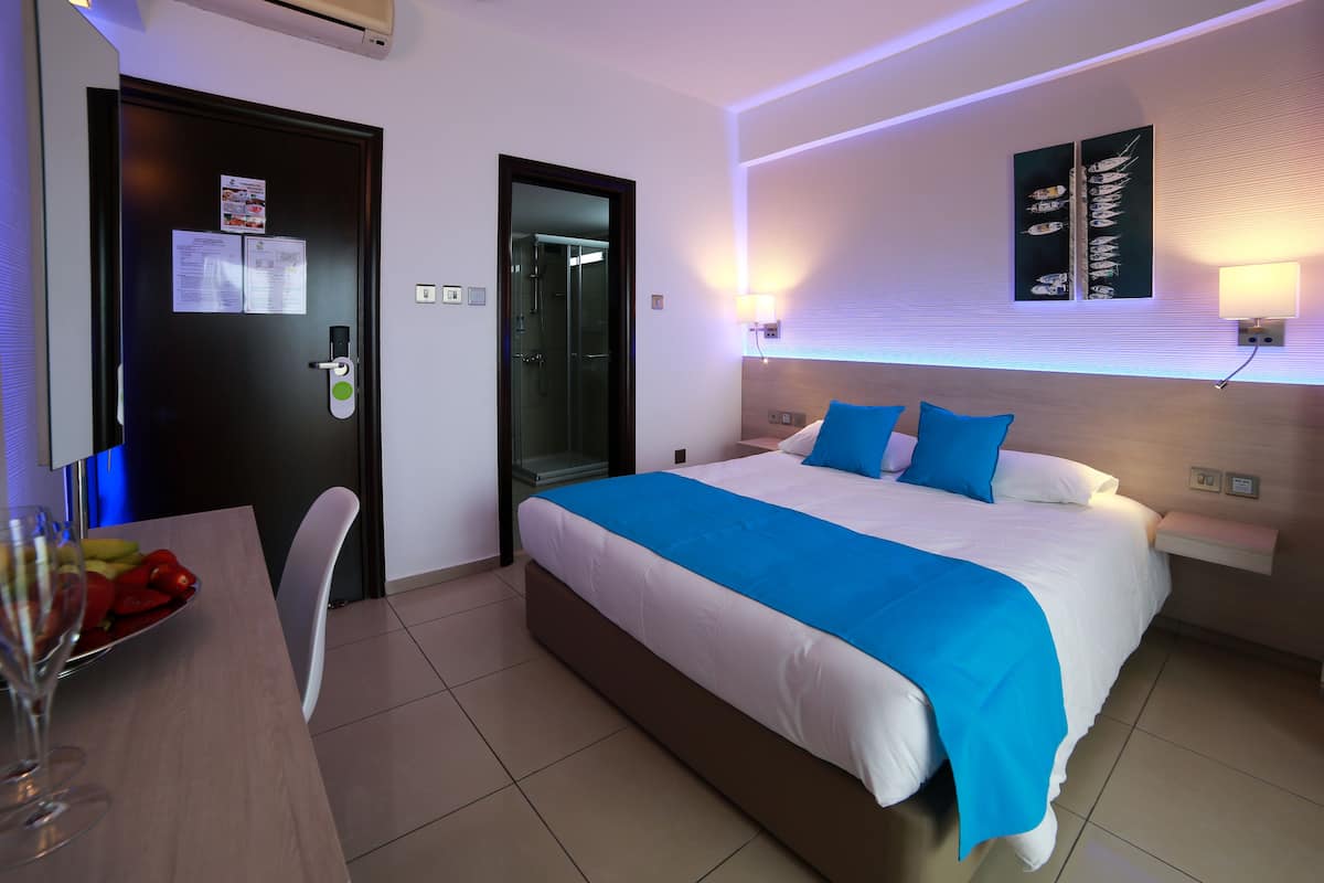 Ein Hotelzimmer mit einem Bett, einem Schreibtisch mit Obstschale, einem Stuhl und einer Tür mit Schloss und Schlüssel.