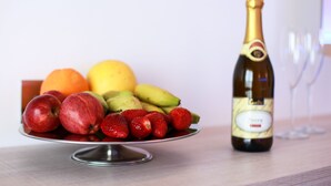 Un panier de fruits contenant des pommes, des fraises et des bananes, ainsi qu’une bouteille de champagne sur une table.