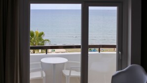 Un balcon avec vue sur la mer, des chaises blanches et une petite table.