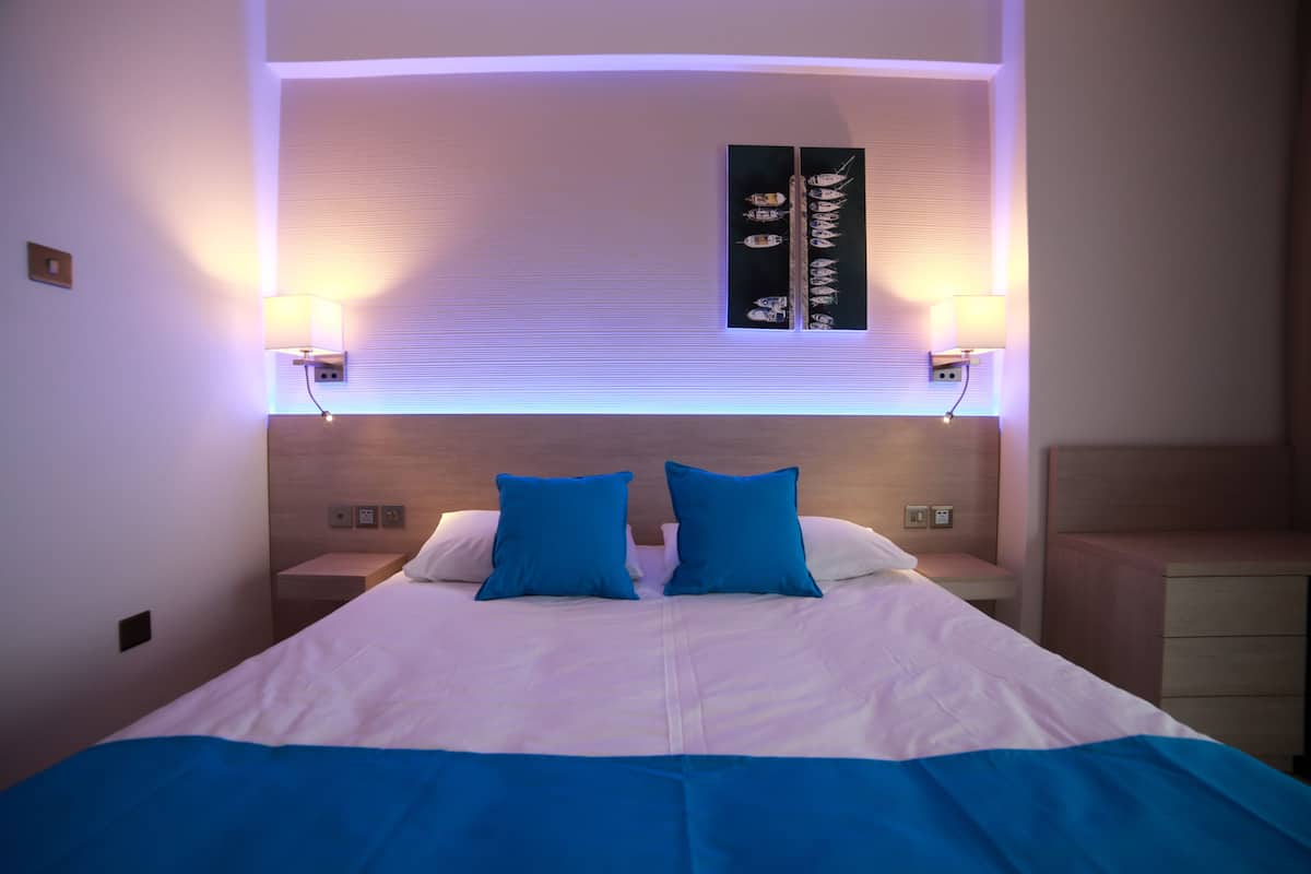 Ein Hotelzimmer mit einem großen Bett, zwei blauen Kissen, einem Nachttisch und Wandlampen.