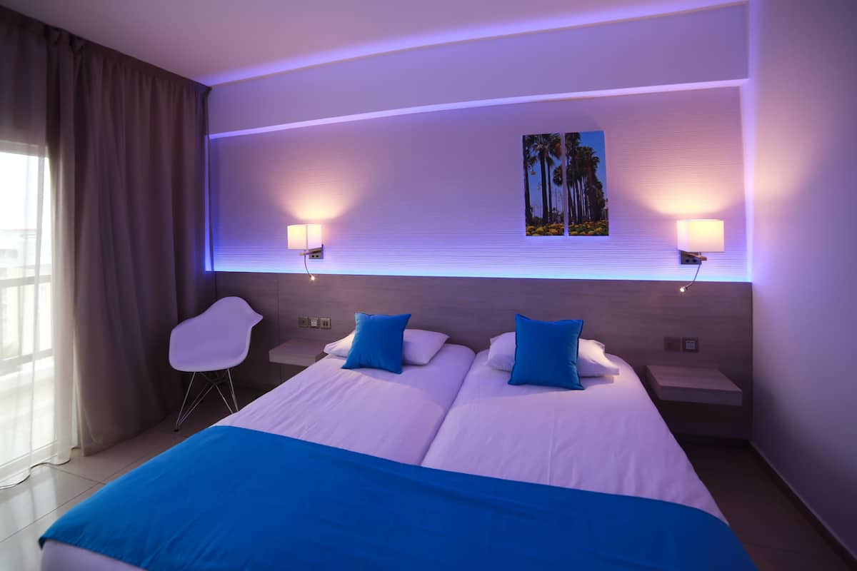 Ein Hotelzimmer mit einem großen Bett, zwei Nachttischen, einem Sessel und einem an der Wand hängenden Bild.