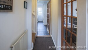 A hallway with a radiator, a framed sign, and a door with glass panels. - Maidstone Family Homes - Fernhill (Maidstone)