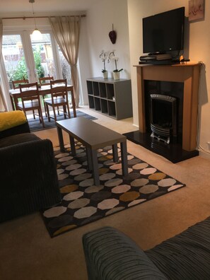 A living room with a fireplace, a television, and a dining area with a table and chairs. - Maidstone Family Homes - Fernhill (Maidstone)