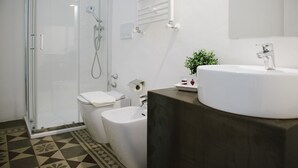 A modern bathroom with a glass shower enclosure, a toilet, a bidet, and a sink with a mirror above it. - Agatha Hotel (Catania)