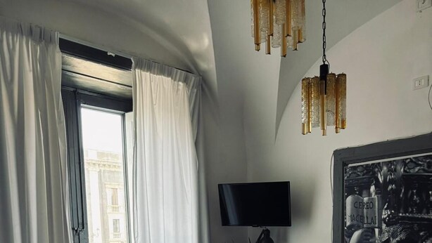 A hotel room with a large bed, a desk with a flat-screen TV, a chair, and a painting on the wall. - Agatha Hotel (Catania)