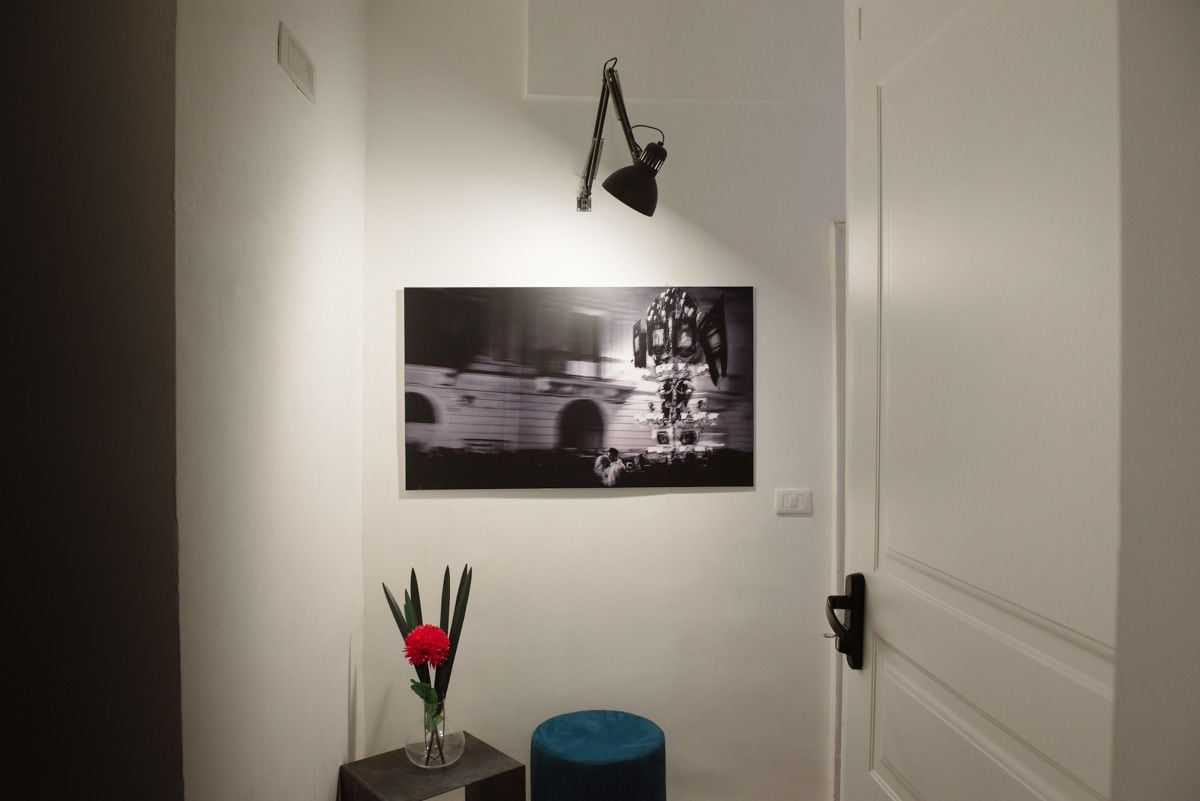 Un pasillo con una fotografía blanco y negro enmarcada en la pared, una mesita con un florero y un otoman azul.