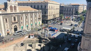A historic building with classical architecture, a busy street with cars and pedestrians, and a clear sky. - Agatha Hotel (Catania)