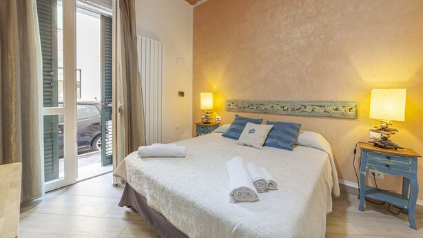 A hotel room with a bed, two bedside tables, a door leading to a balcony, and a view of a parked car outside. - Prima dell'Elba Bed & Breakfast (Piombino)