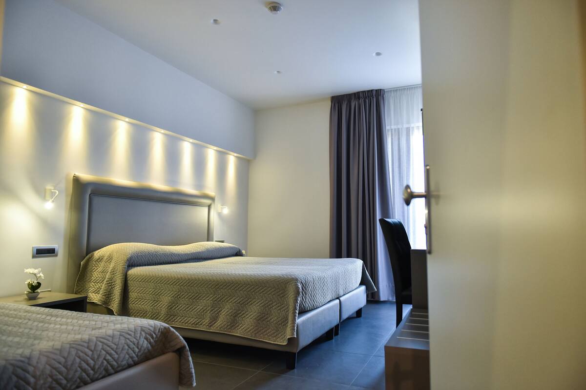 A hotel room with two beds, a large window with curtains, and a modern headboard.